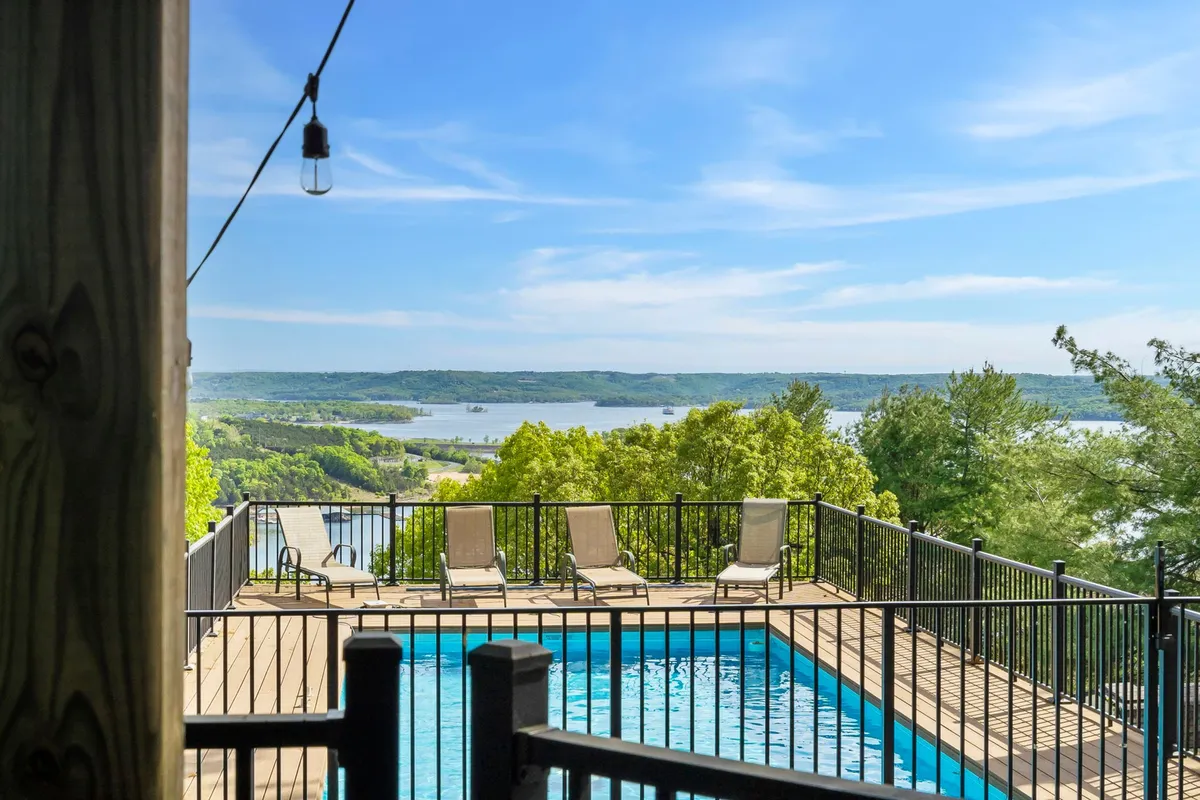 A serene outdoor space showcases a sparkling swimming pool surrounded by lounge chairs, abundant greenery, and an unobstructed view of the lake. The ambiance is calm, with soft evening light hinting at sunset possibilities.