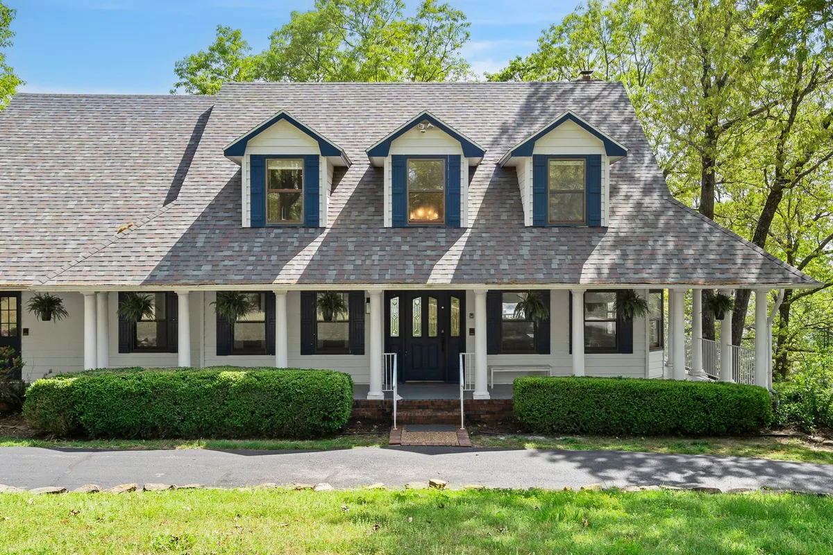 This image captures the elegant front porch of the home, highlighting its charming architectural features, landscaped bushes, and inviting windows. The porch is bathed in natural light, suggesting a serene spot to relax and soak in the surroundings.