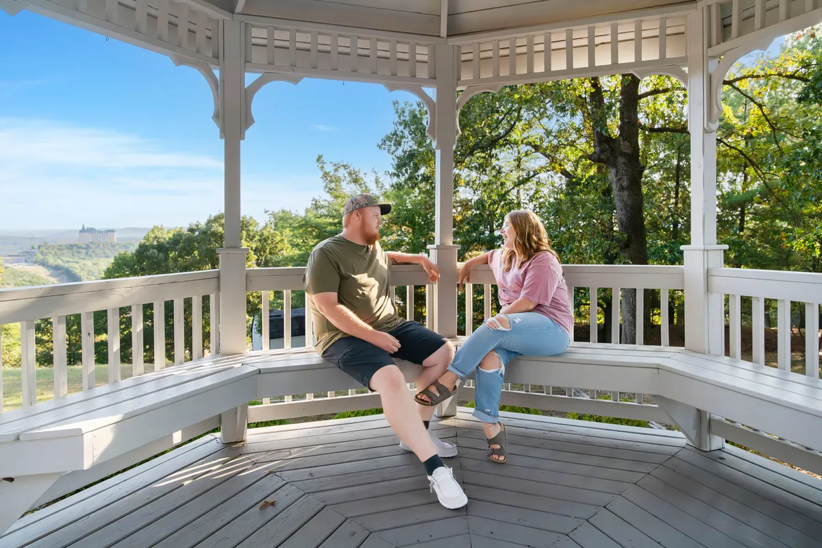 A romantic gazebo is nestled amid lush greenery, with a couple enjoying a peaceful moment and panoramic views of the surrounding landscape and horizon. The atmosphere is one of quiet relaxation and intimacy, inviting guests to create memories outdoors.