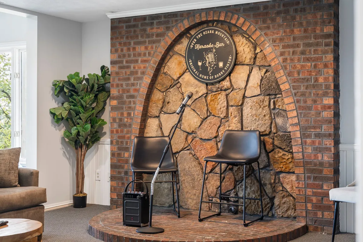 A karaoke microphone sits ready beside a stone fireplace and stylish bar stools, setting the stage for lively singalongs and casual gatherings. The cozy yet vibrant atmosphere hints at memorable nights of entertainment.