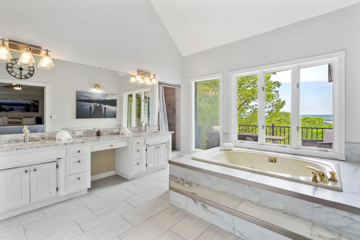 A tranquil ensuite bathroom with a deep soaking bathtub, double vanity, marble countertops, and expansive windows letting in natural light. The space feels spa-inspired and offers a sense of privacy and indulgence.