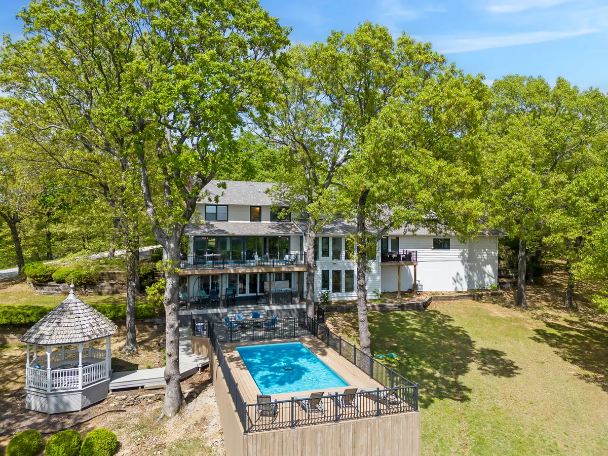 The pool area is complemented by a beautiful gazebo with a grill underneath, set on a wooden deck shaded by mature trees. In the background are the house and lush landscaping, with intimate seating areas inviting outdoor dining and social gatherings.