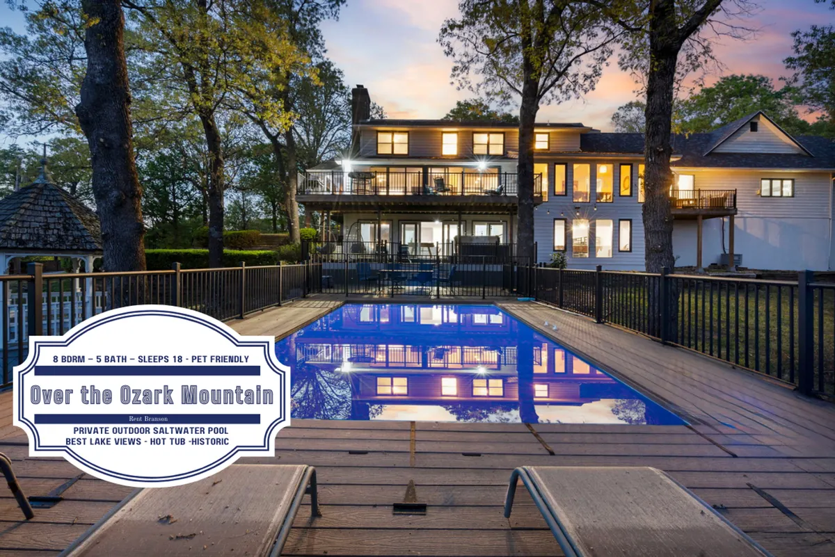 A luxurious saltwater pool sits at the center, surrounded by a spacious deck with lounge chairs and outdoor seating. Behind the pool, there's a panoramic view of the tranquil lake and distant mountains. The back of the house is visible, seamlessly connecting indoor spaces to the inviting outdoor retreat.