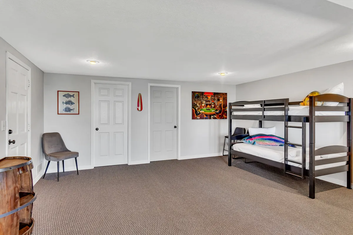 A playful and inviting bunkroom adorned with bunk beds, colorful artwork, a wooden barrel, and a cozy chair. The space feels casual and perfect for younger guests or families seeking a fun sleepover.