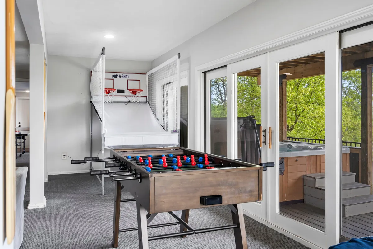 A bright rec room features a foosball table and basketball arcade game, with large windows letting in plenty of sunlight. The space is energetic and inviting, designed for spirited games and family bonding.
