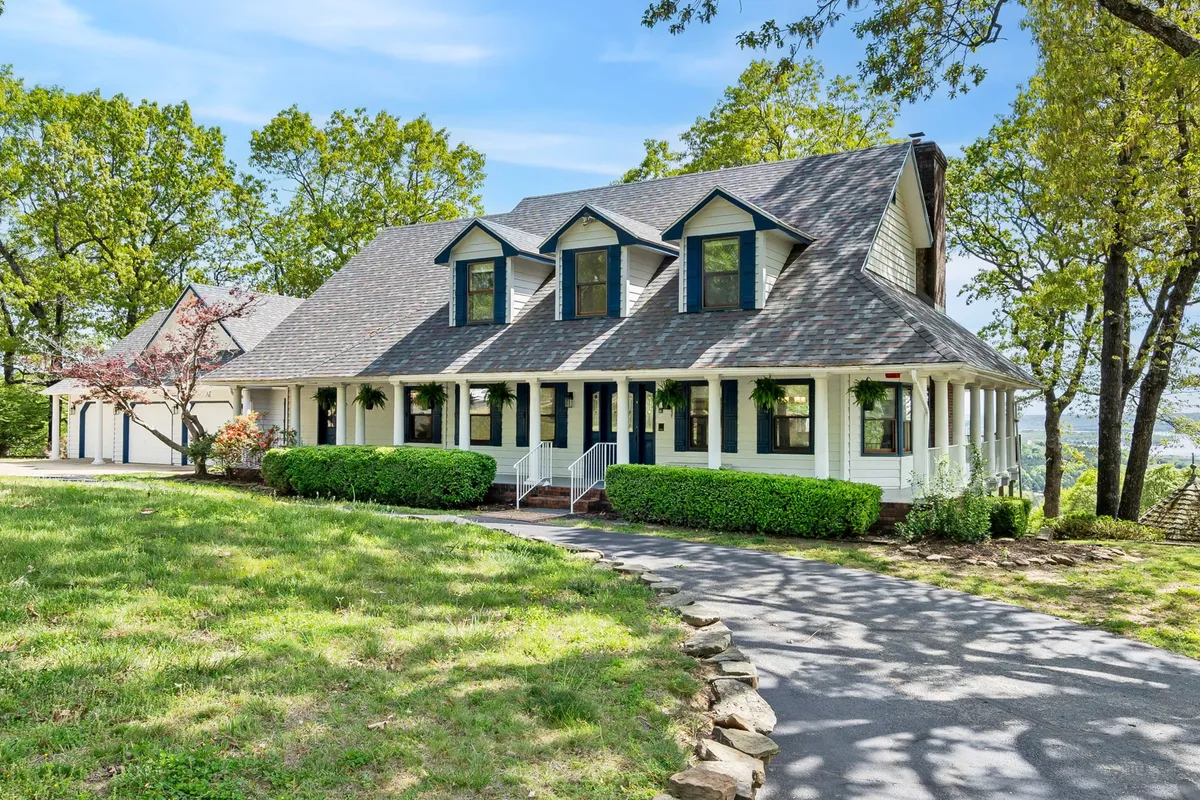 The exterior shot highlights the wrap-around front porch, distinctive roofline, and lush surroundings. The porch is ready for gatherings, offering a tranquil transition from the outdoors into the welcoming interior spaces.
